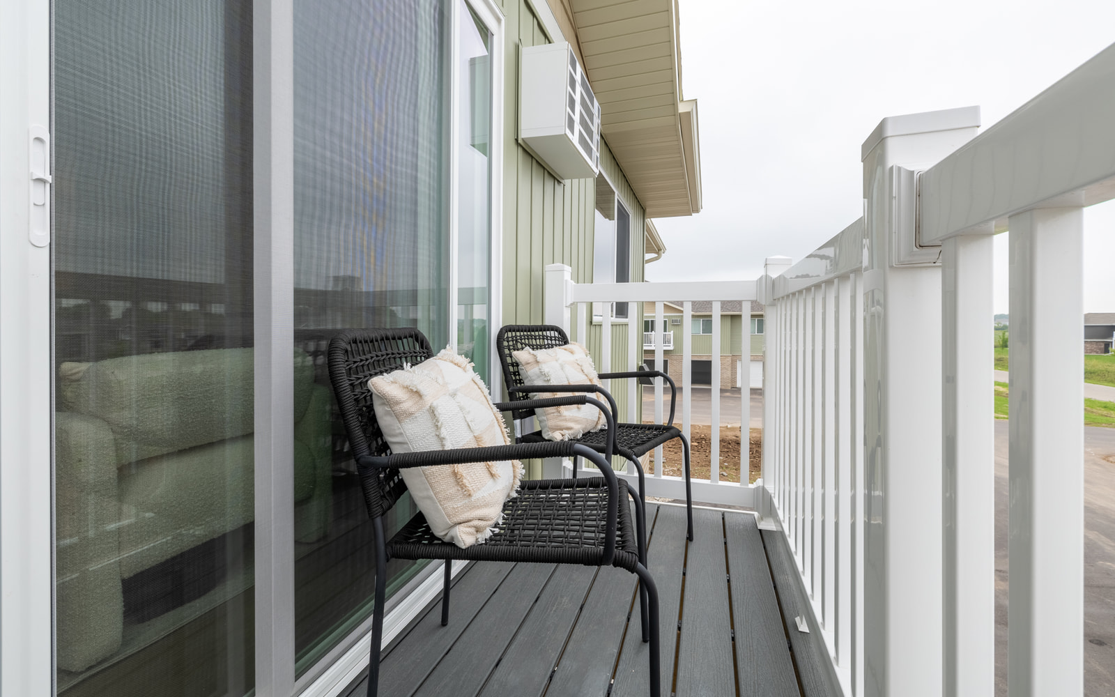 Private balcony with white railing and two black woven chairs with cream pillows, outside a sliding glass door