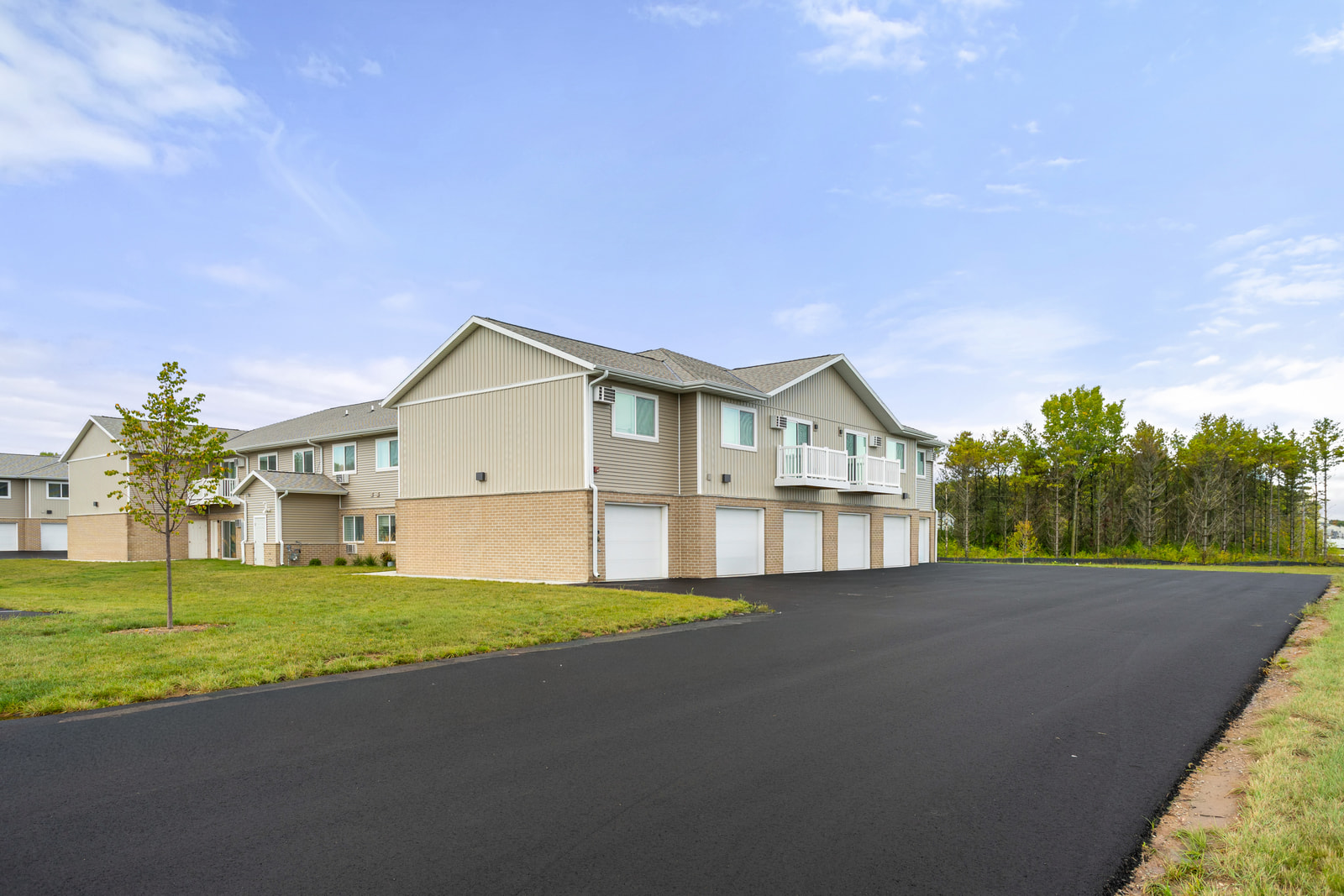 Exterior of the building with tan siding, brick base and a row of white garage doors, beside a newly paved driveway